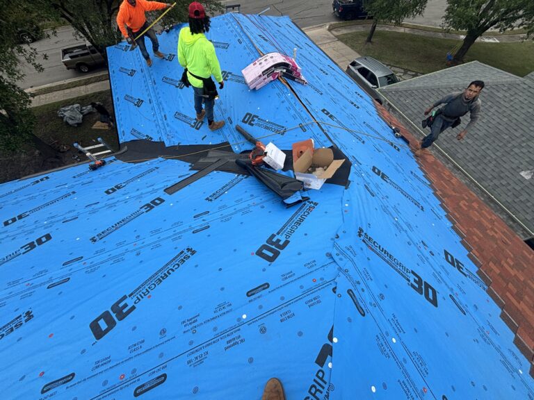 Roofing crew working on intersecting roof slopes covered with blue underlayment