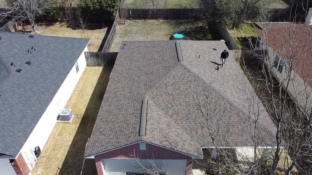 Overhead view of a shingle roof with ridges, vents and a person on the roof