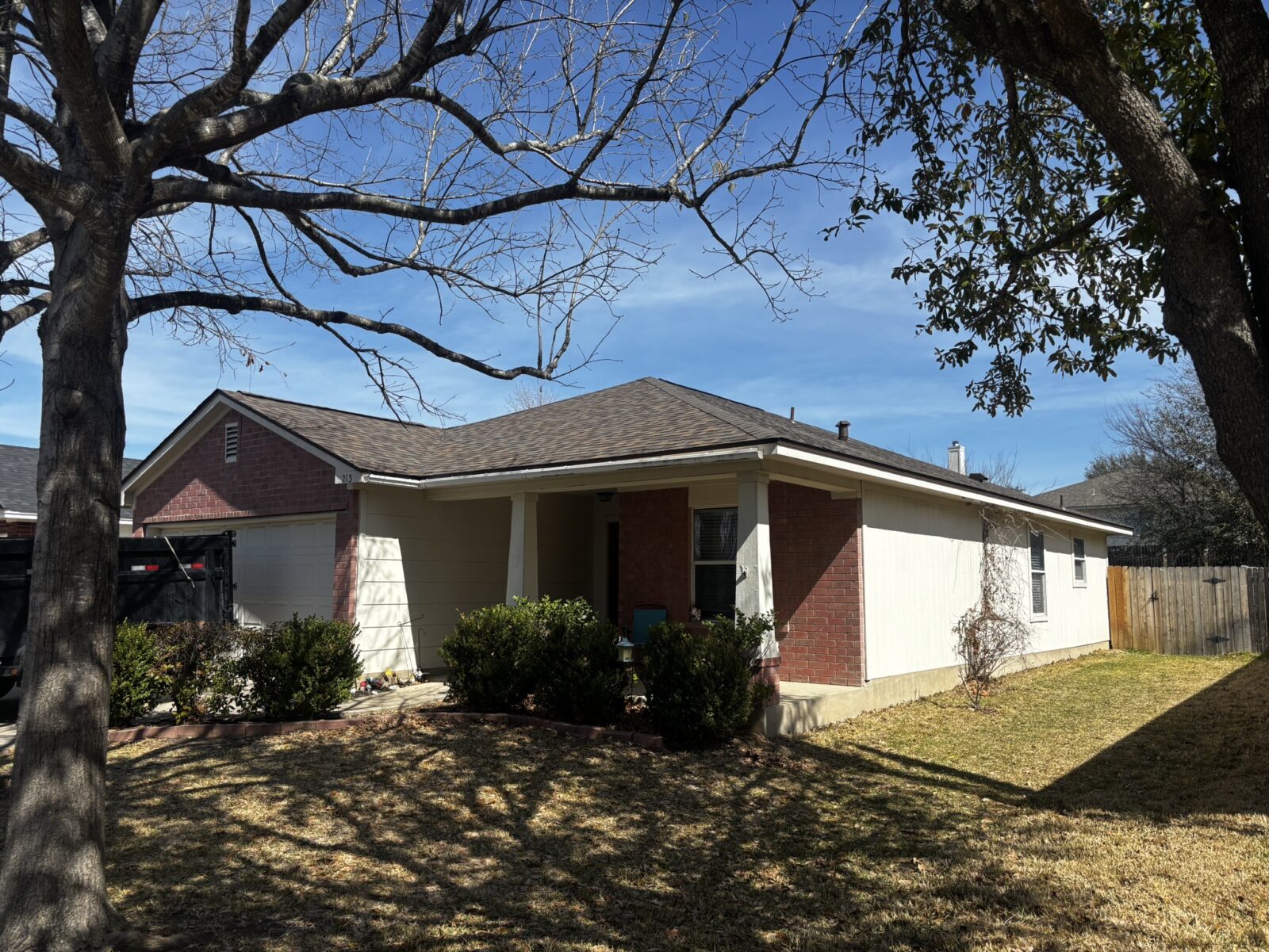 Shingle roof and front of a home framed by mature tree branches