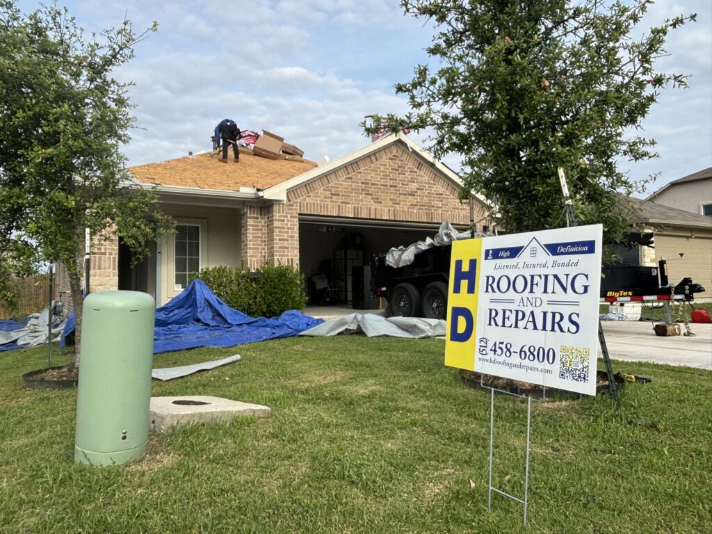Roof work with exposed wood decking, workers and an HD Roofing sign in the yard